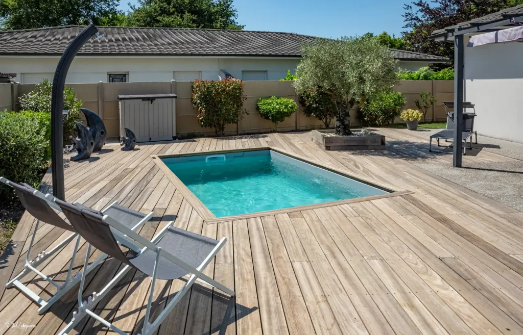 Rechthoekig minibad op een groot houten terras met ligstoelen en een tuin