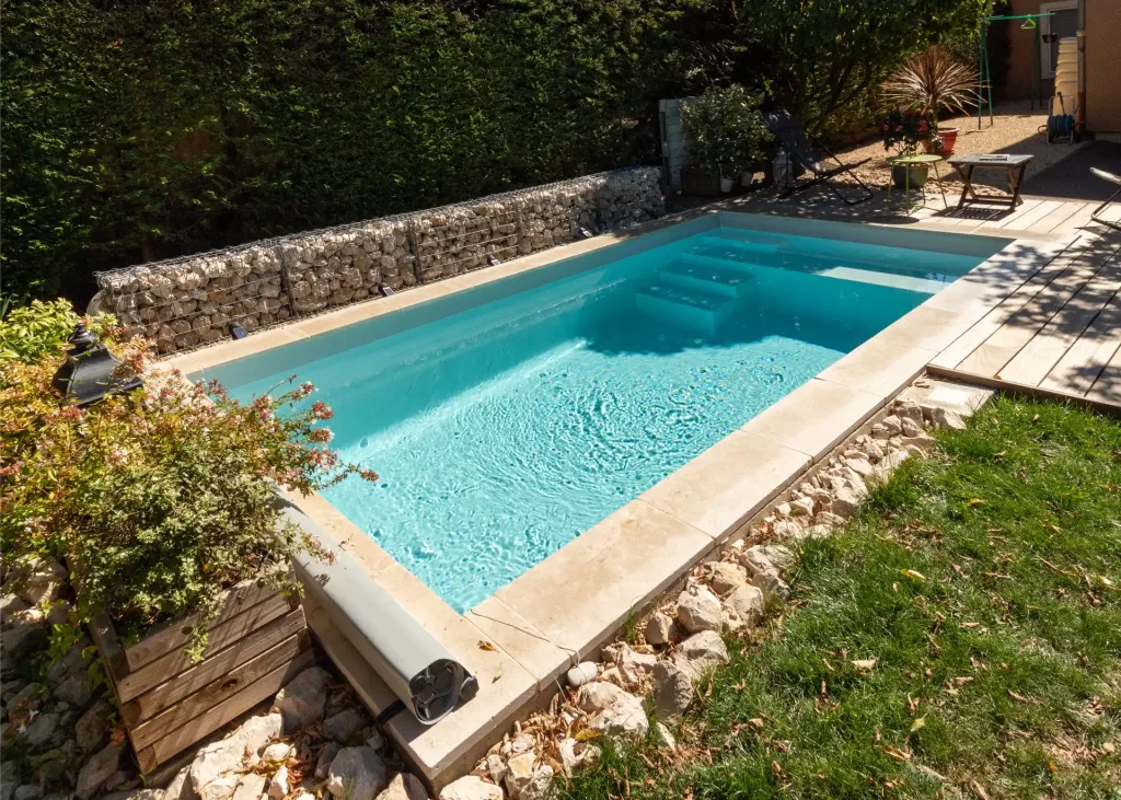 Piscine rectangulaire turquoise avec escalier, vue de côté sur terrasse en pierre et gazon