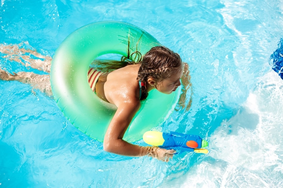 Enfant jouant dans une piscine coque avec un pistolet à eau et une bouée gonflable verte