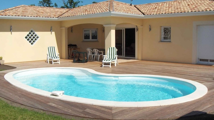 Vue sur une piscine coque polyester en haricot, intégrée dans une terrasse en bois