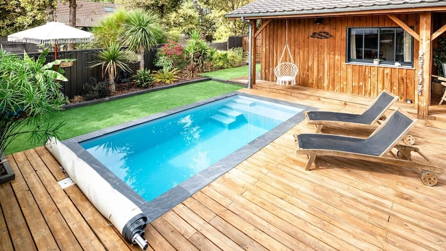Vue sur une piscine coque polyester rectangle, intégrée dans un jardin fleuri